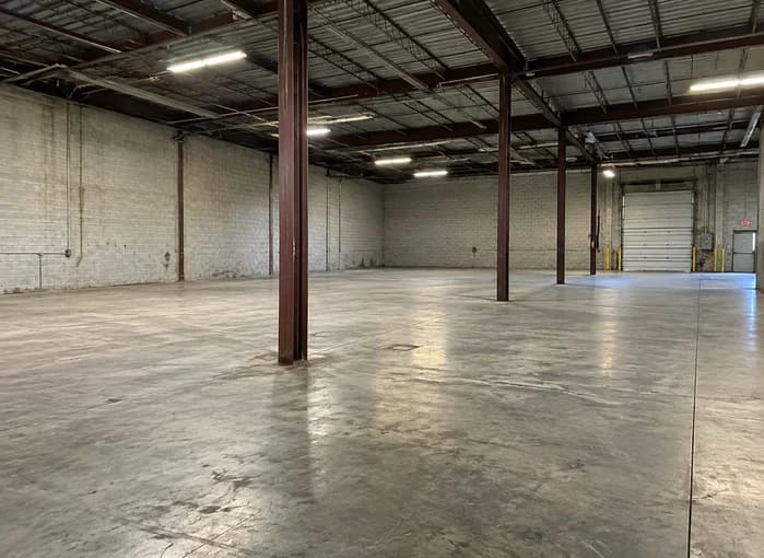 Open warehouse area with an existing concrete slab, steel columns and exposed roof structure before interior build-out
